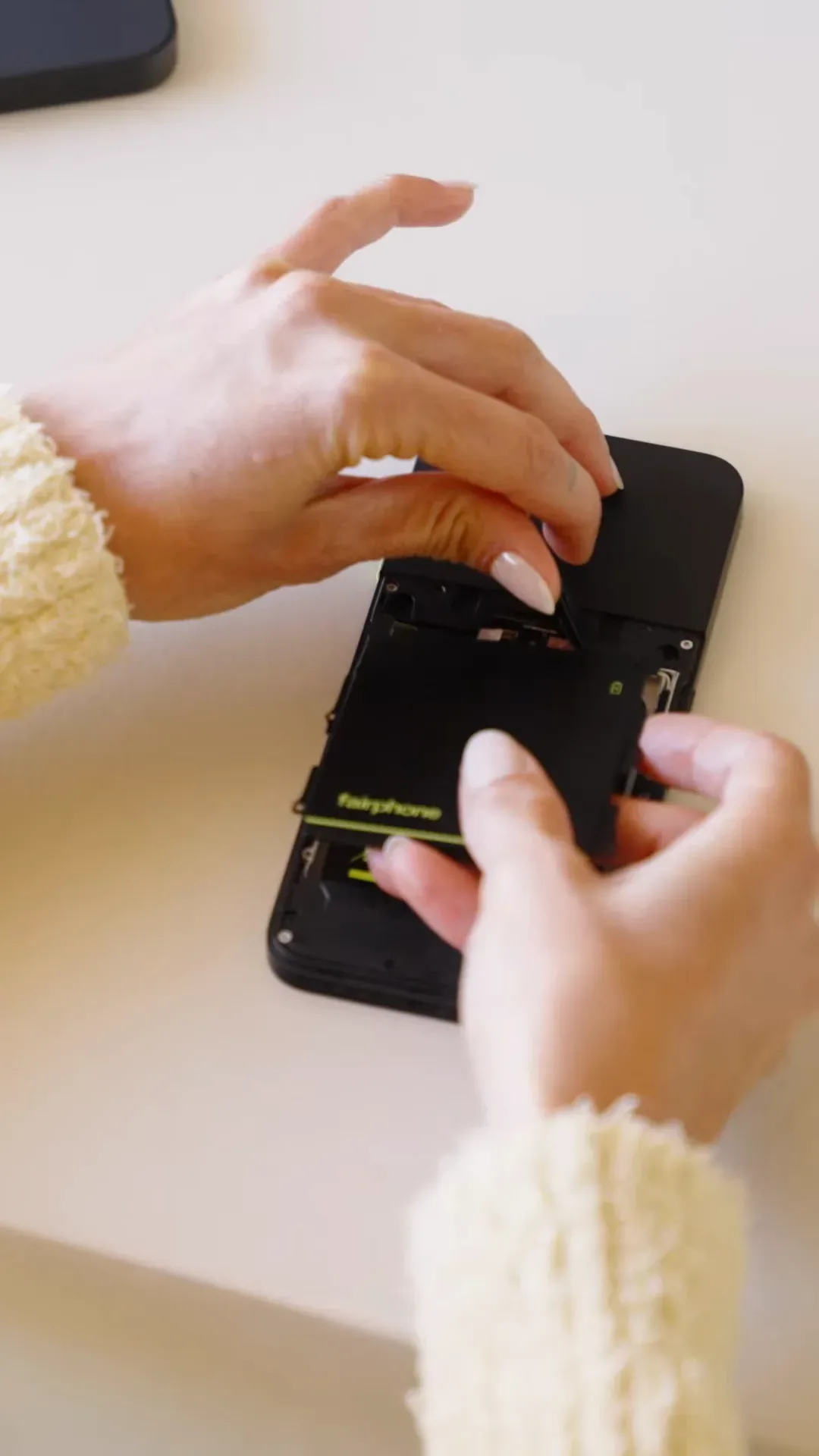 Hands repairing a Fairphone 6 at a table, lifting out a module with a small screwdriver nearby